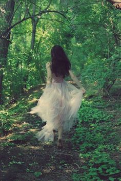 a woman in a dress walking through the woods