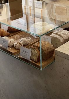 an assortment of breads and pastries on display in a glass case at a bakery