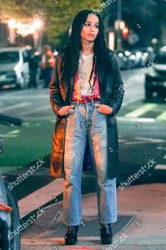 a woman with long black hair is standing on the sidewalk