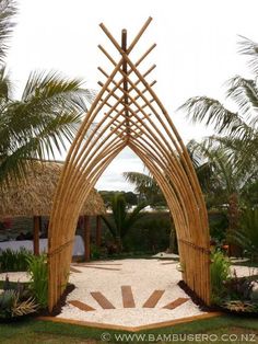 an arch made out of bamboo sticks and stones in the middle of a garden with palm trees