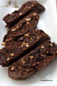 some brownies are on a white plate and one is cut in half with nuts