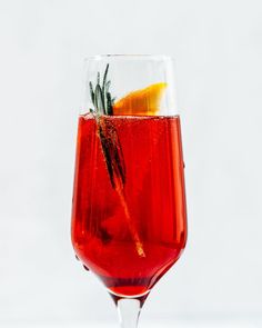 a glass filled with red liquid and garnished with an orange slice