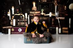 a little boy sitting on top of a suitcase in front of a harry potter backdrop