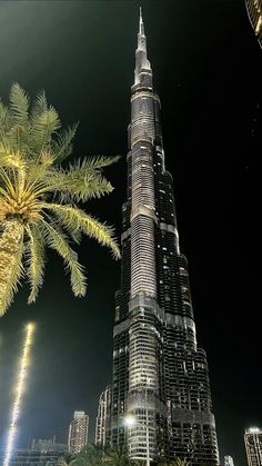 the burj building is lit up at night with palm trees in front of it