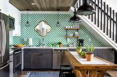 a kitchen with green and white tiles on the wall, wood flooring and stainless steel appliances