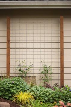 an outside view of a house with flowers and plants in the foreground, along with a fence on the other side