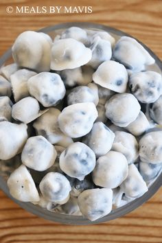 a glass bowl filled with white mushrooms on top of a wooden table next to a spoon