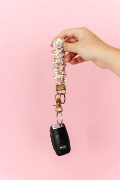 a hand holding a car key chain with a cell phone attached to it on a pink background