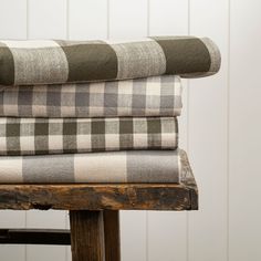 a stack of plaid blankets sitting on top of a wooden chair next to a white wall