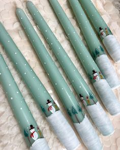 six green candles with snowmen on them are lined up in a row and sitting on a white doily