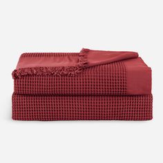 the red sheets and blankets are folded on top of each other, both with fringes