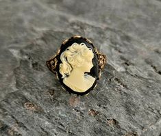 A gorgeous detailed cameo with a black background and cream relief set in detailed antiqued brass. Ring is antiqued brass with an adjustable, detailed band. Details: Ring measures 20mm x 15mm Ring band is adjustable, sizes 6 - 8-1/2 Ring is plated brass Lead & Nickel free Cameo is hard, matte resin Please allow for possible slight color differences due to different settings on different screens. Thank you for shopping Delicate Industry :)