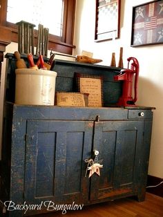 an old blue cabinet with many items on top and some writing on the bottom, in front of a window