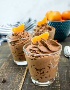 three desserts with chocolate frosting and orange slices on the top one is in a glass bowl