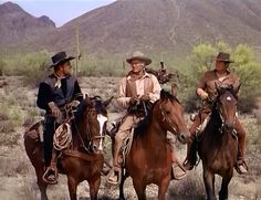 three men in cowboy hats are riding horses