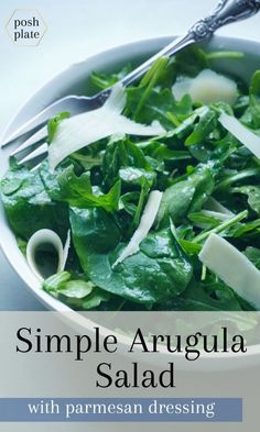 a white bowl filled with greens and cheese on top of a blue tablecloth next to a fork