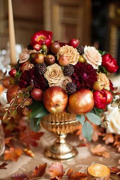 a vase filled with apples and flowers on top of a table covered in fall leaves