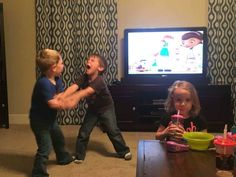 two young children playing video games in front of a flat screen tv on the entertainment center