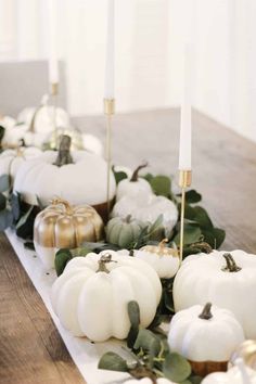 white pumpkins and greenery are arranged on a long table with candles in the middle