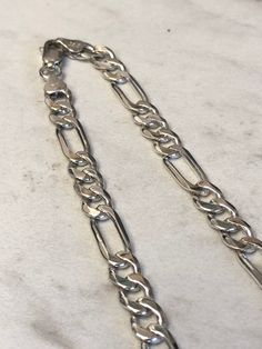 "Sterling Silver Unisex Solid Link Figaro Chain Necklace 18\" in Length. This chain is very flexible and comfortable to wear with its shiny bright plain polished finish. This chain has finished end caps and a lobster claw clasp closure and is 7mm wide and weighs 28.1 grams. This item would Retail for $429.00" Sterling Silver Figaro Chain Jewelry, Silver Metal Jewelry With Figaro Chain, Silver Bracelet With Figaro Chain And Oval Link, Silver Sterling Jewelry With Figaro Chain, White Gold Sterling Silver Figaro Chain Bracelets, White Gold Sterling Silver Bracelets With Figaro Chain, White Gold Sterling Silver Bracelet With Figaro Chain, Silver Figaro Chain Bracelet As Gift, Sterling Silver Figaro Chain Jewelry Gift