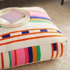 a colorful striped ottoman with a white plate on it and a pink card in the middle