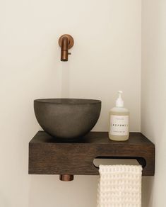 a bowl sink sitting on top of a wooden shelf next to a white towel and soap dispenser