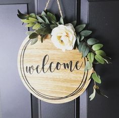 a welcome sign hanging on the front door with flowers and greenery around it that says welcome