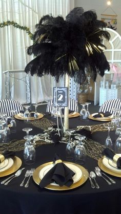 a table set with black and gold plates, silverware and a palm tree centerpiece