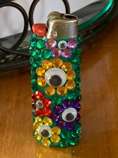 a lighter with many different colored stones on it sitting on a table next to some scissors