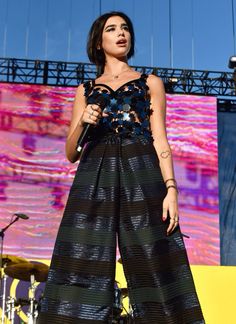 a woman standing on top of a stage with her hands in her pockets and holding a microphone