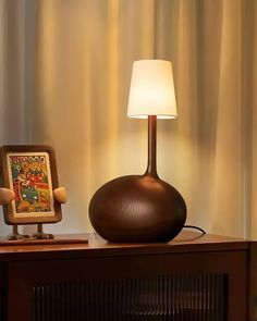 a table lamp sitting on top of a wooden shelf next to a small framed painting