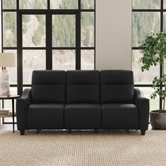 a black leather couch sitting in front of large windows next to a table with a potted plant