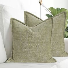 two pillows sitting on top of a white couch next to a green potted plant