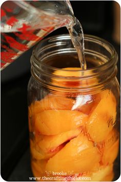 a glass jar filled with sliced peaches and water pouring from a pitcher into it