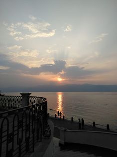 the sun is setting over the water and some people are standing on the shore line