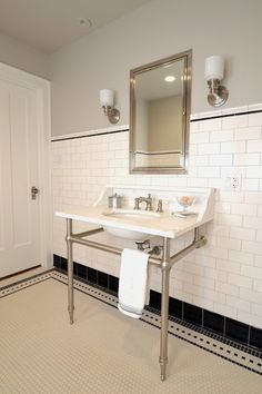 a white bathroom with black and white tile on the floor, two sinks and a mirror