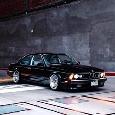 a black car parked on the street next to a brick wall and cement flooring