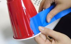 someone is cutting out a piece of blue paper from a red and white coffee cup