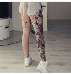 a woman with tattoos on her leg standing in front of a mirror and looking at the floor