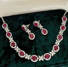 A luxurious Ruby Red and Diamond necklace set for the gorgeous woman, lusciously crafted with American diamonds and ruby stones. Perfect for any occasion.  Details: Necklace Width-0.5 Inches Earrings Length-1.75 Inches Weight of Each Earring- 4.5 grams All products are manufactured using traditional skills from our rich heritage of crafts.  The process of these crafts is essentially manual. Hence, any irregularities or variations are an inherent part of these handcrafting processes. Ruby Round-shaped Jewelry Sets For Anniversary, Dazzling Red Necklaces With Sparkling Stones, Ruby Necklaces With Sparkling Stones For Wedding, Formal Ruby Jewelry Sets With Sparkling Stones, Ruby Necklace With Sparkling Stones For Wedding, Wedding Ruby Necklace With Sparkling Stones, Hand Set Ruby Jewelry Sets, Hand Set Ruby Jewelry Sets For Anniversary, Red Bridal Necklace With Sparkling Stones For Wedding