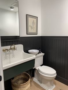 a white toilet sitting next to a sink in a bathroom under a framed painting on the wall