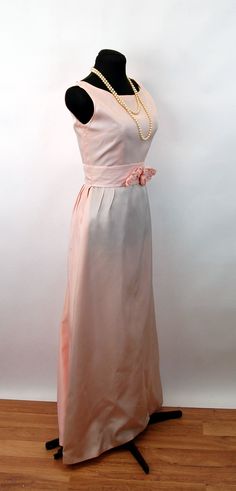 "This 1960s gown is simply elegant, with a detachable panel. The panel attaches to the waist via wrapping around and securing with two snaps. There is a pretty fabric flower and leaves sewn onto the front. The bodice is fitted, with a bateau neckine. The skirt is lined with netting to add body. A metal zipper is up the center back. No labels. Good condition. There is a light rose colored mark on the back just under the neckline. Would make a very pretty bridesmaid's dress. Measurements - Bust - Pink Satin Gown With Pleated Bodice, Elegant Pink A-line Vintage Dress, 1950s Style Vintage Wedding Dress, 1950s Style A-line Wedding Dress, Pink Pleated Bodice Evening Dress For Wedding, Pink Evening Dress With Pleated Bodice For Wedding, Pink Bridesmaid Gown With Pleated Bodice, Pink Gown With Pleated Bodice For Spring, Vintage Pink Ball Gown Dress