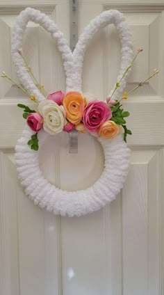 a white wreath with pink and orange flowers hanging on the front door, decorated with bunny ears