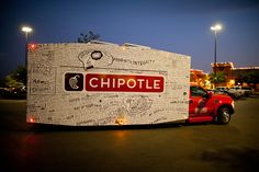 a red truck parked in a parking lot next to a building with chipotle written on it