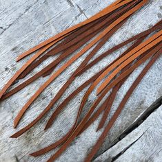 brown leather fringes are laid out on a piece of weathered wood, ready to be used in crafts