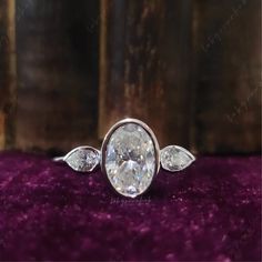 an oval diamond ring with three pear shaped diamonds on the side and two leaves around it