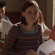 a young woman sitting at a table in front of two other people writing on paper