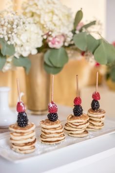 small pancakes with berries and blackberries on top are displayed in front of a vase