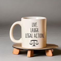 a white coffee mug with the words live laugh legal action on it sitting on a wooden coaster