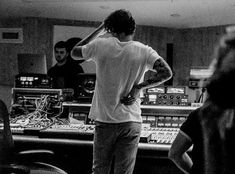 a man standing in front of sound mixing equipment with his back to the camera, while people look on